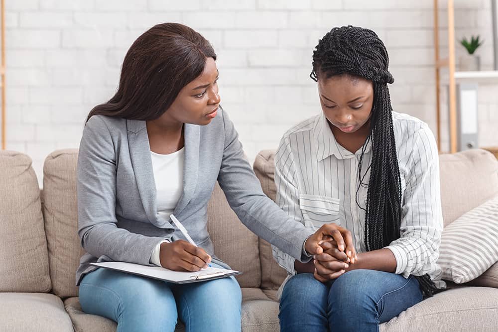 Psychologist comforting depressed female patient during therapy session in office